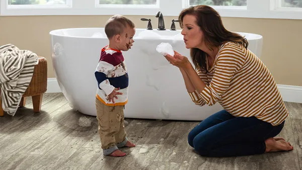 Una madre está arrodillada en el piso del SPC para bañar a su bebé.