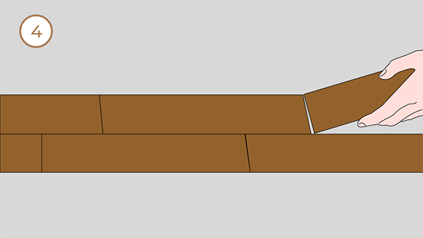 There are two rows of flooring on the ground, and a hand is laying a piece.