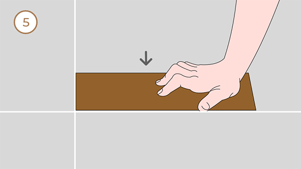 A hand installing a piece of flooring along the line.