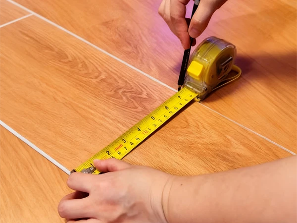 Workers are using a tape measure to measure and mark the SPC flooring.