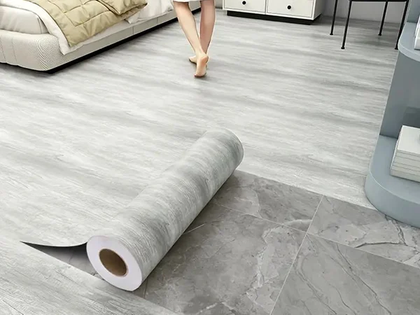 Rolling out the gray wood-grain SPC flooring on the marble ceramic tiles in the bedroom.