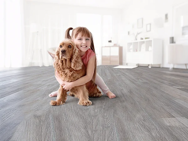 A little girl sits cross-legged on scratch-resistant, pet-proof SPC flooring, cuddling her playful dog.