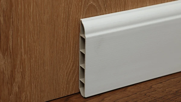 El skirting SPC gris está montado en un piso de madera marrón